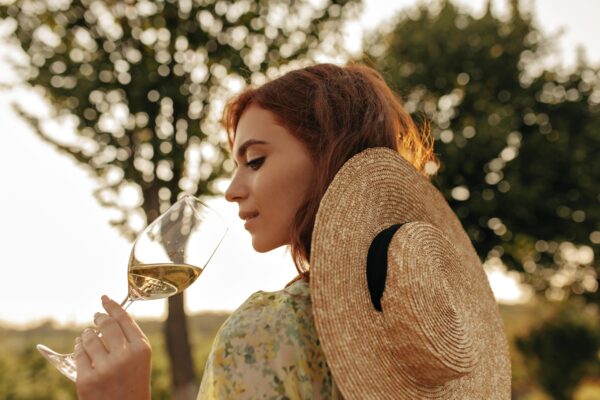 stylish-young-girl-with-foxy-hairstyle-modern-straw-hat-cool-summer-outfit-posing-with-glass-with-champagne-outdoor-min